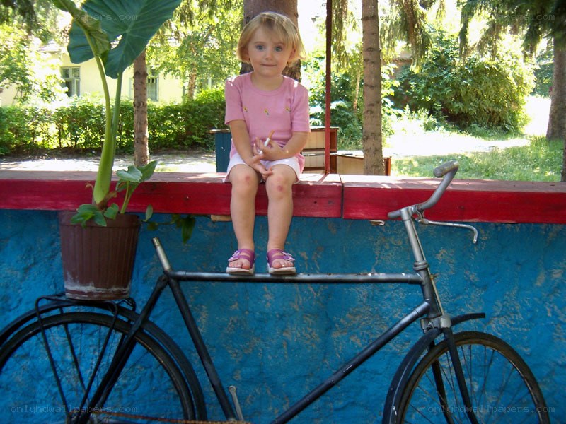 child sitting on a wall with bicycle