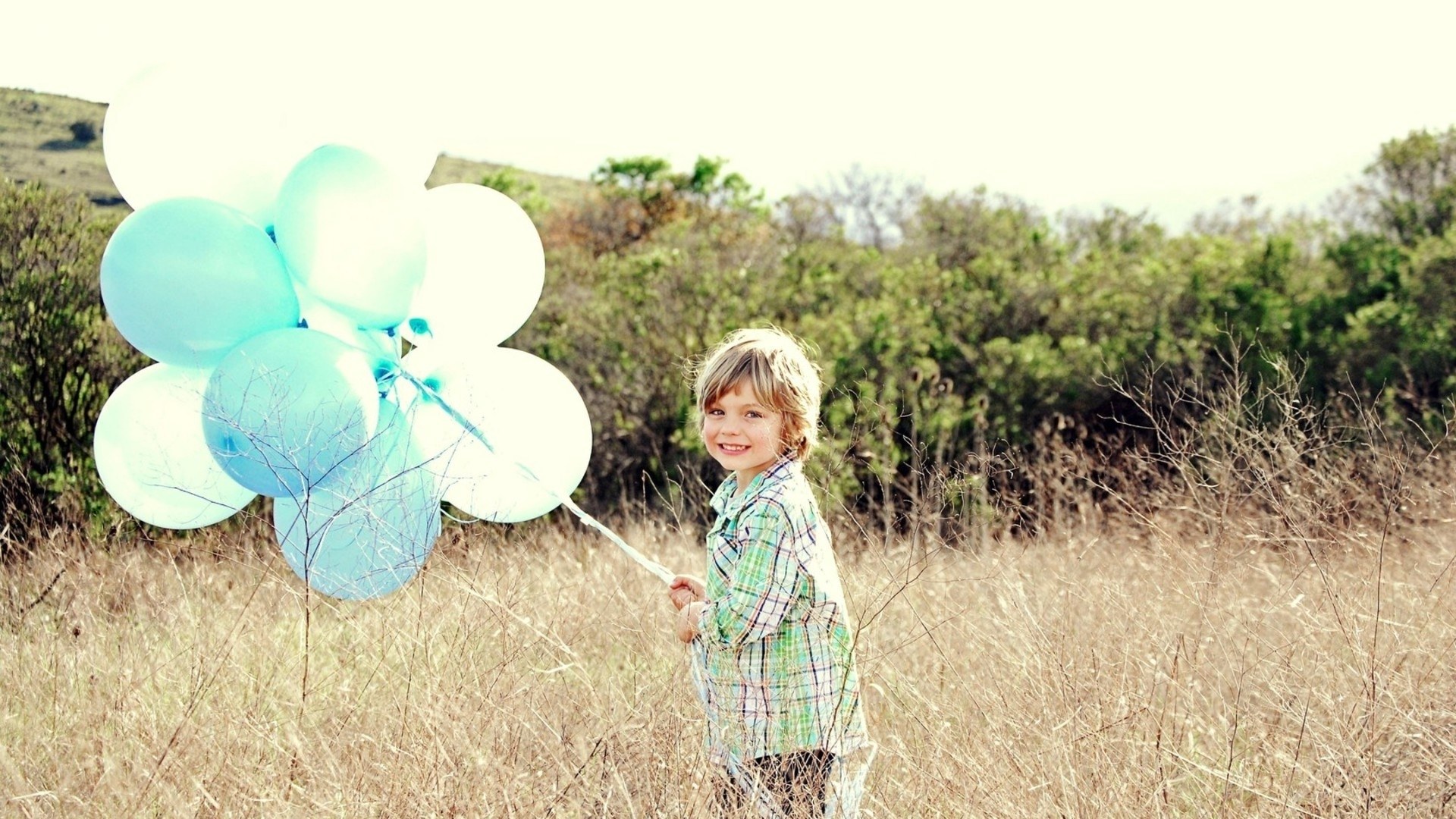 child with balloons in field