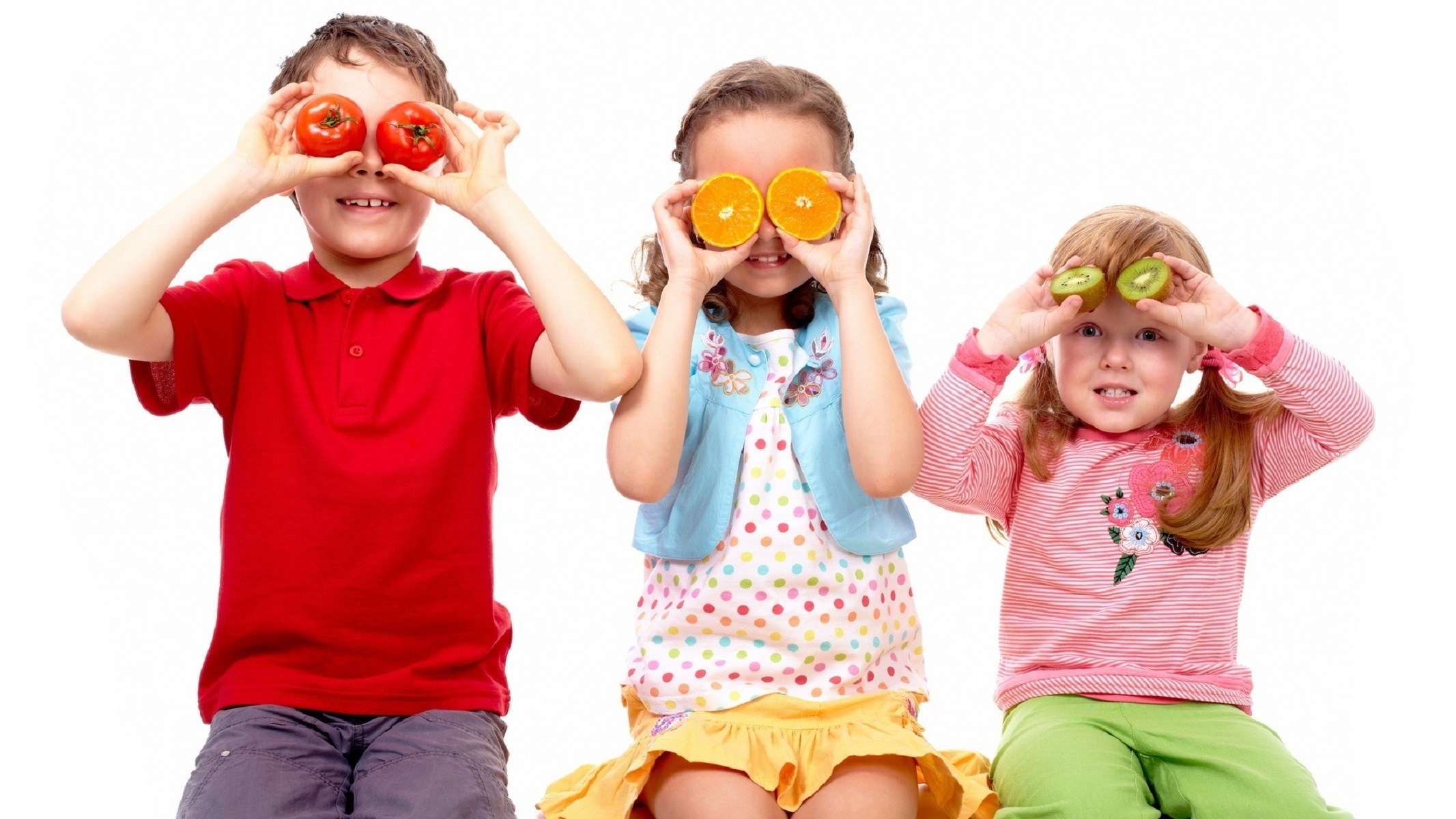 children holding fruit over eyes