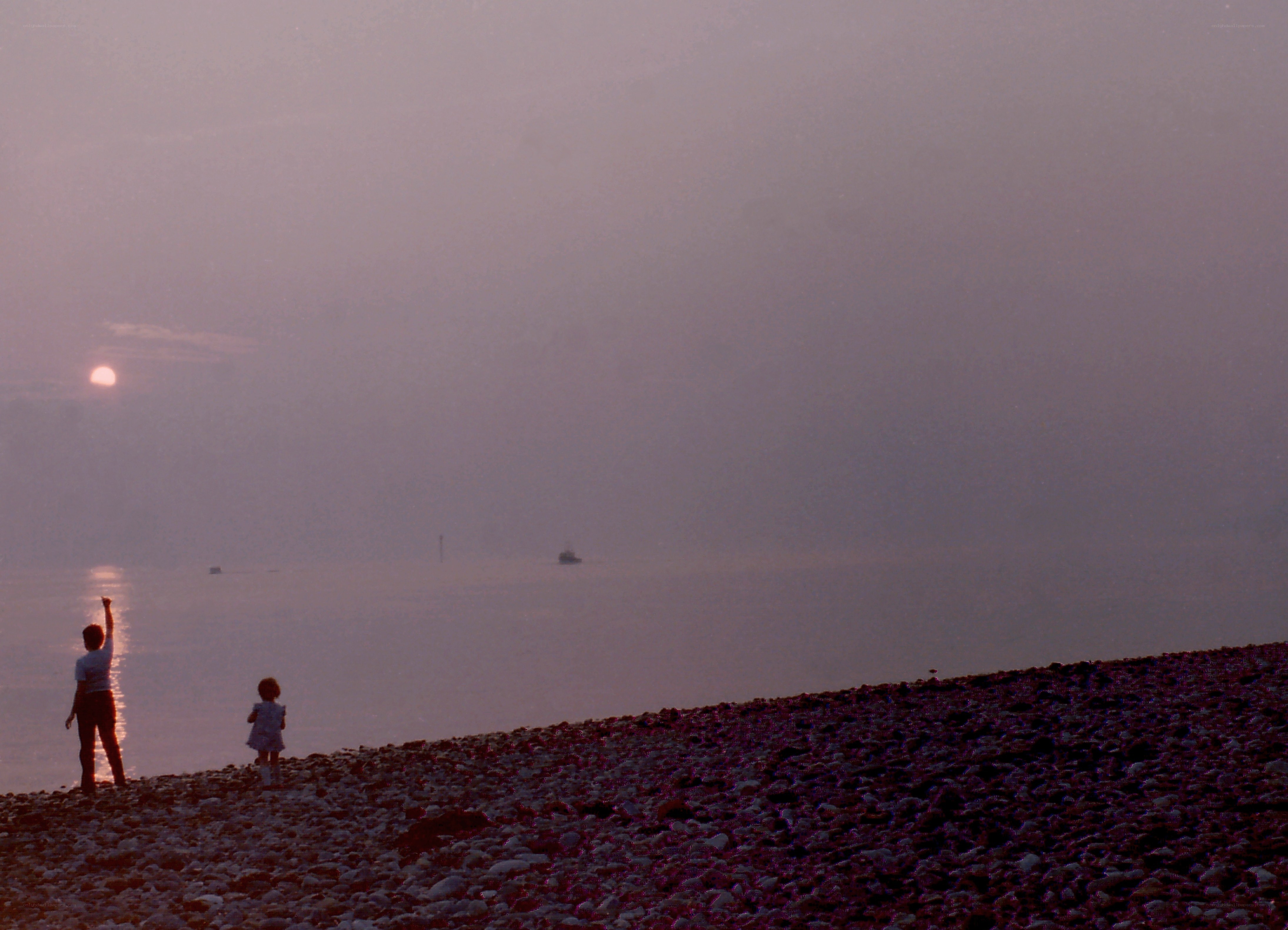 Children on a pebble beach at sunset