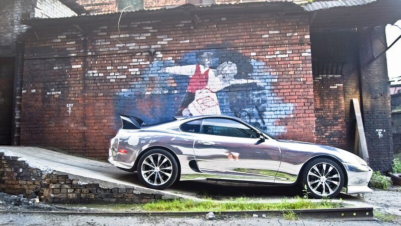 Chrome car in alley with mural