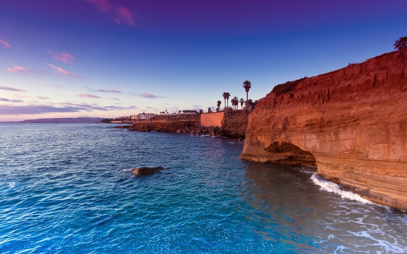 Cliffside Coastline — Blue, Serene, Sunset, Photograph, Ocean, Palm Trees, Buildings