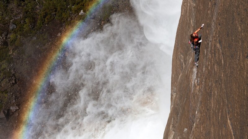 Climber near waterfall with rainbow