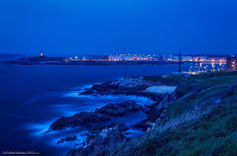 Coastal City at Night — Blue, Serene, Photograph, Lighthouse, Buildings