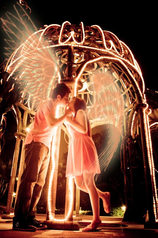 Couple kissing under glowing angel sculpture