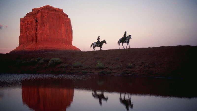 Cowboys on horseback at sunset