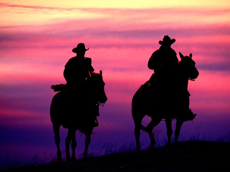 Cowboys on horseback at sunset