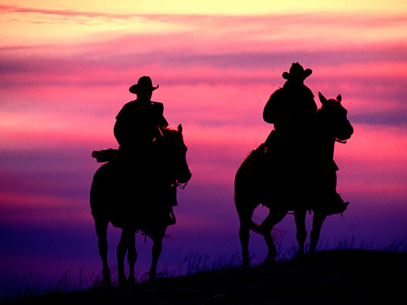 Cowboys on horseback at sunset