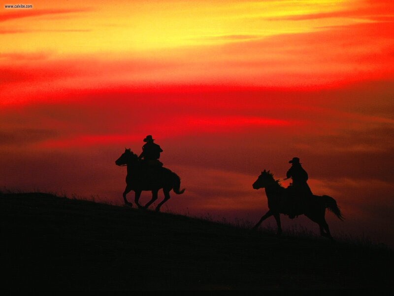 Cowboys on horseback at sunset
