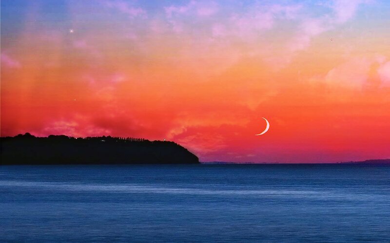 Crescent moon over ocean at sunset