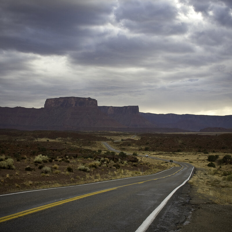 Desert road with mesas under stormy sky