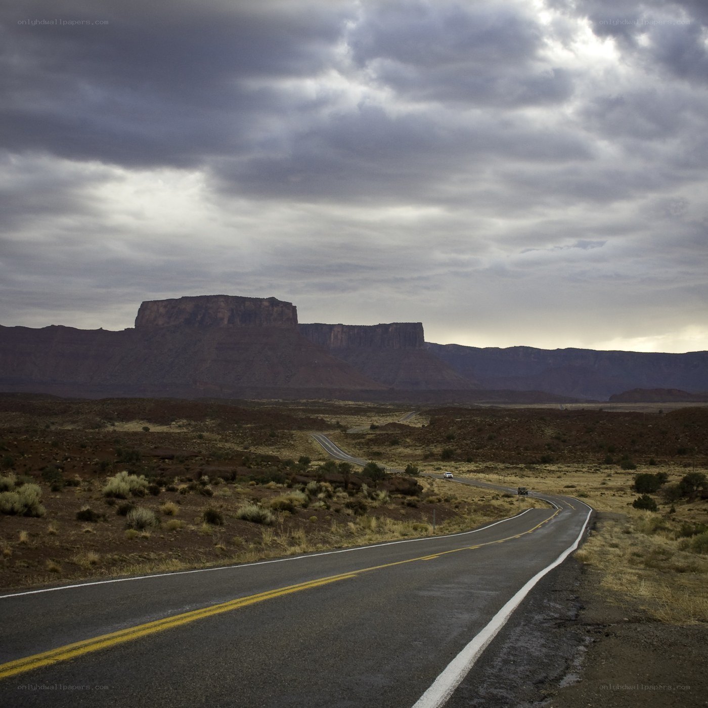 Desert road with mesas under stormy sky
