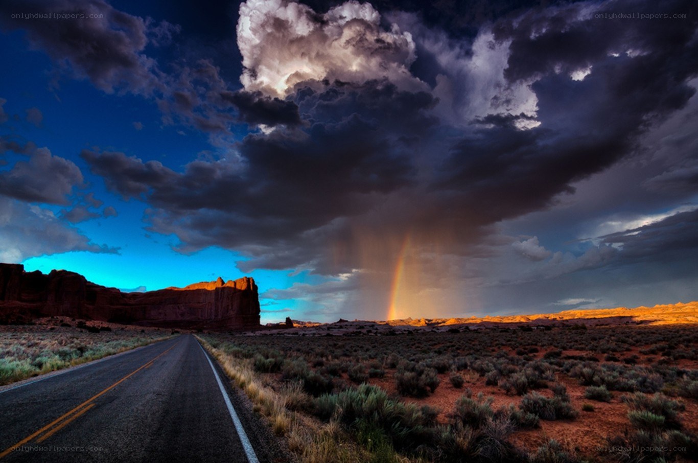 Desert road with storm and rainbow