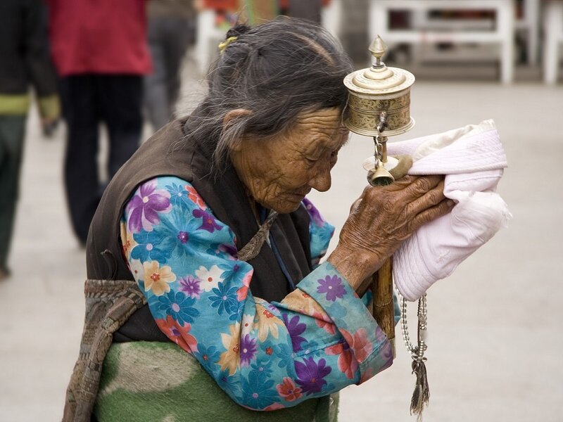 Elder woman praying with a prayer wheel