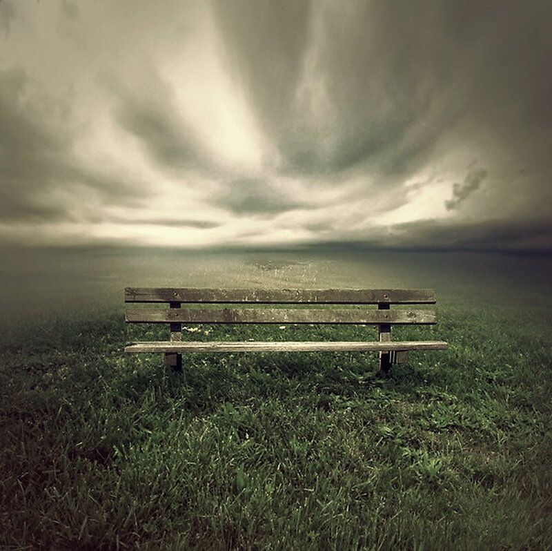 Empty bench under stormy sky