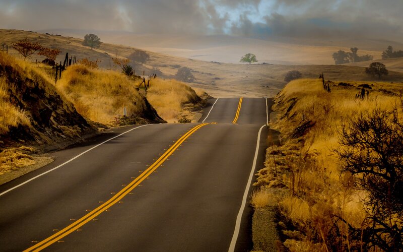Empty road through golden hills