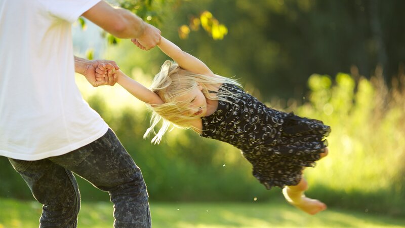 father spinning daughter in park