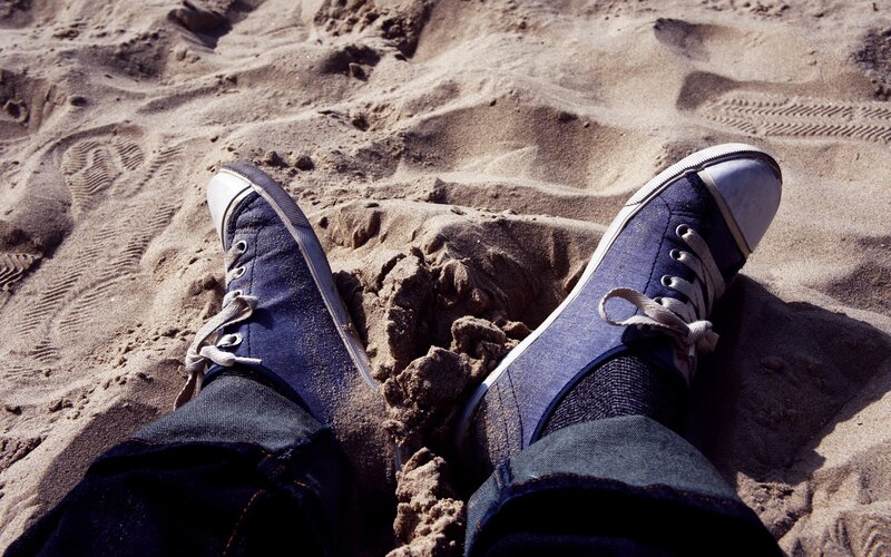 feet in blue sneakers on sand