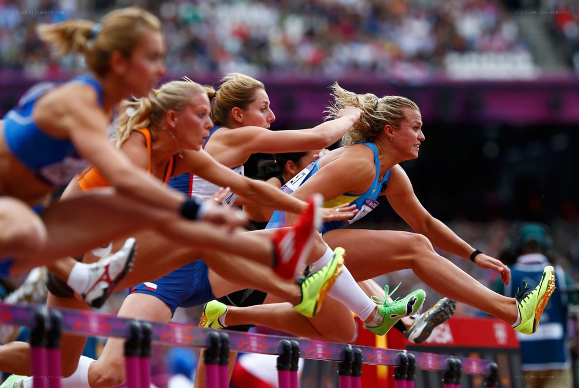 Female athletes jumping hurdles