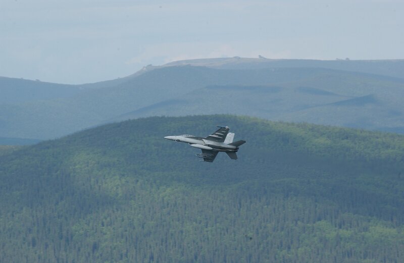 Fighter jet over forested mountains