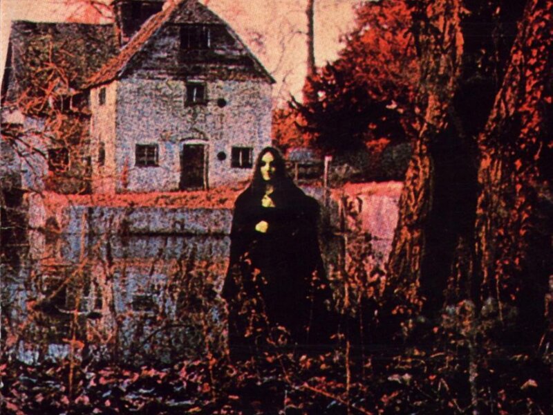 figure in black cloak near house