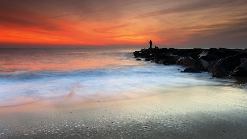 Fisherman at sunset on rocky shore