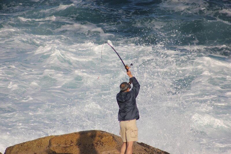 Fisherman casting rod on rocky shore