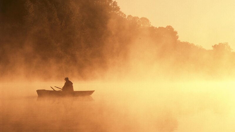 Fisherman on misty lake at dawn