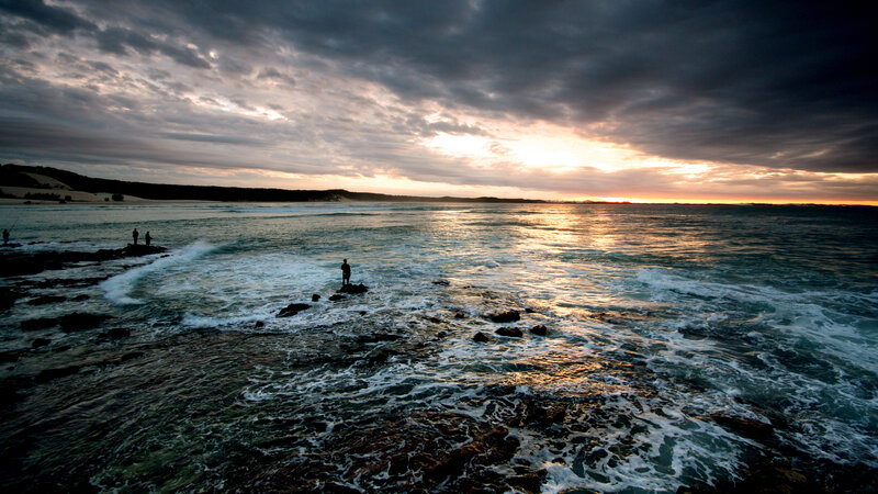 fishermen at sunset on rocky shore