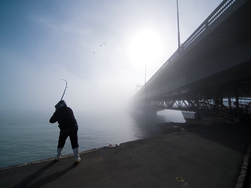 Fishing under a foggy bridge