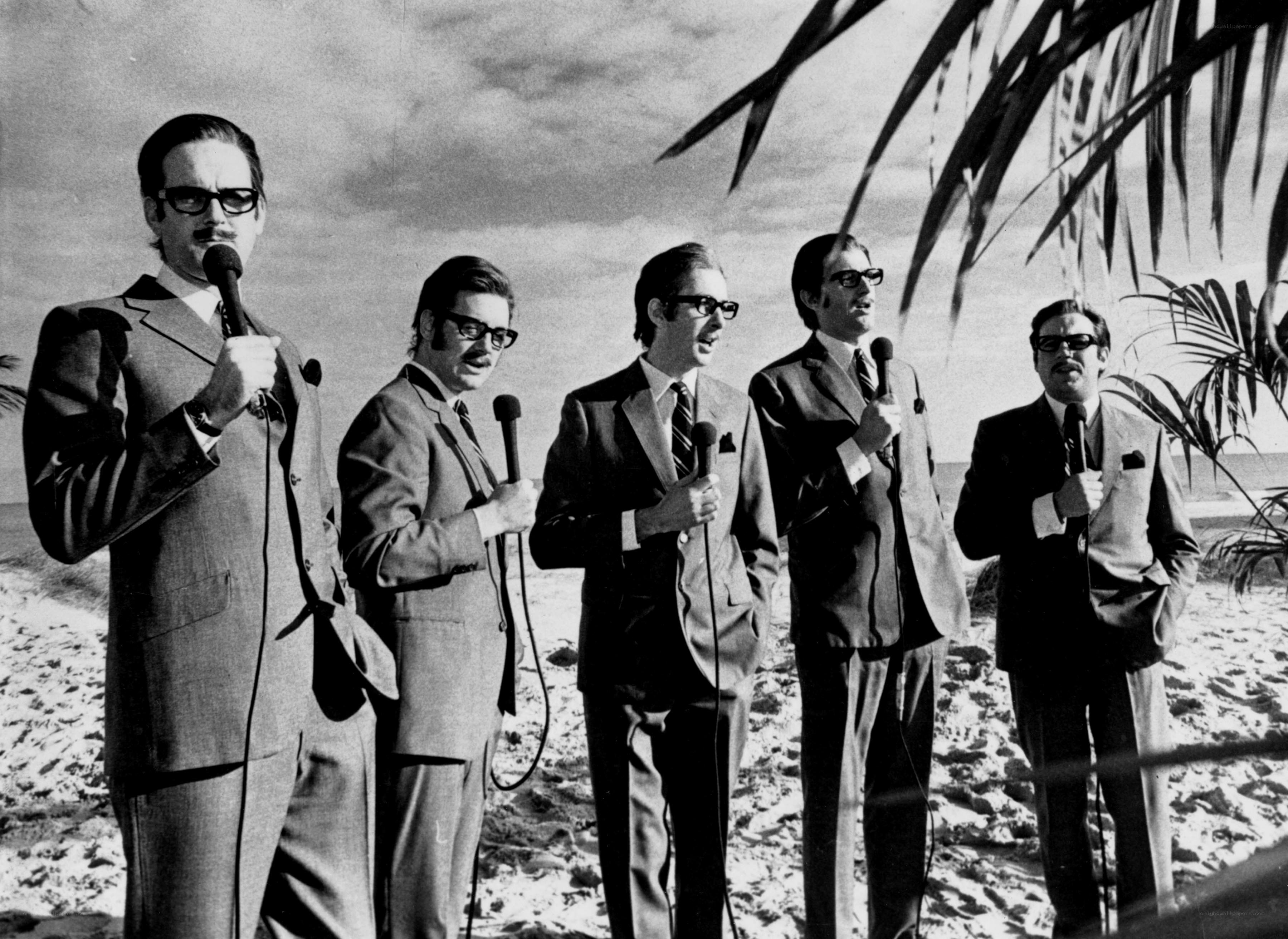 Five men on a beach with microphones