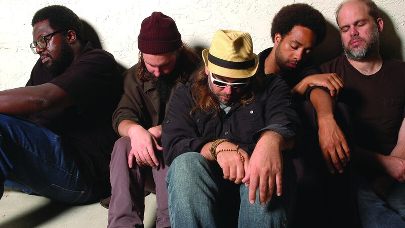 five men sitting against a wall