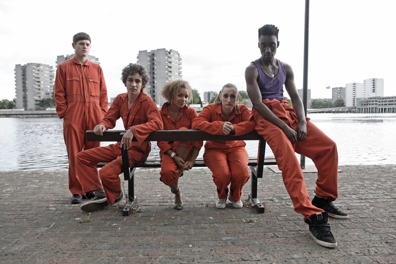 Five people in orange jumpsuits by water