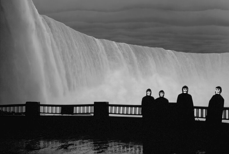 Four figures with skull masks at a waterfall