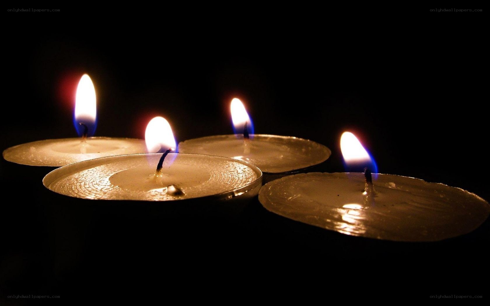 four lit candles in darkness