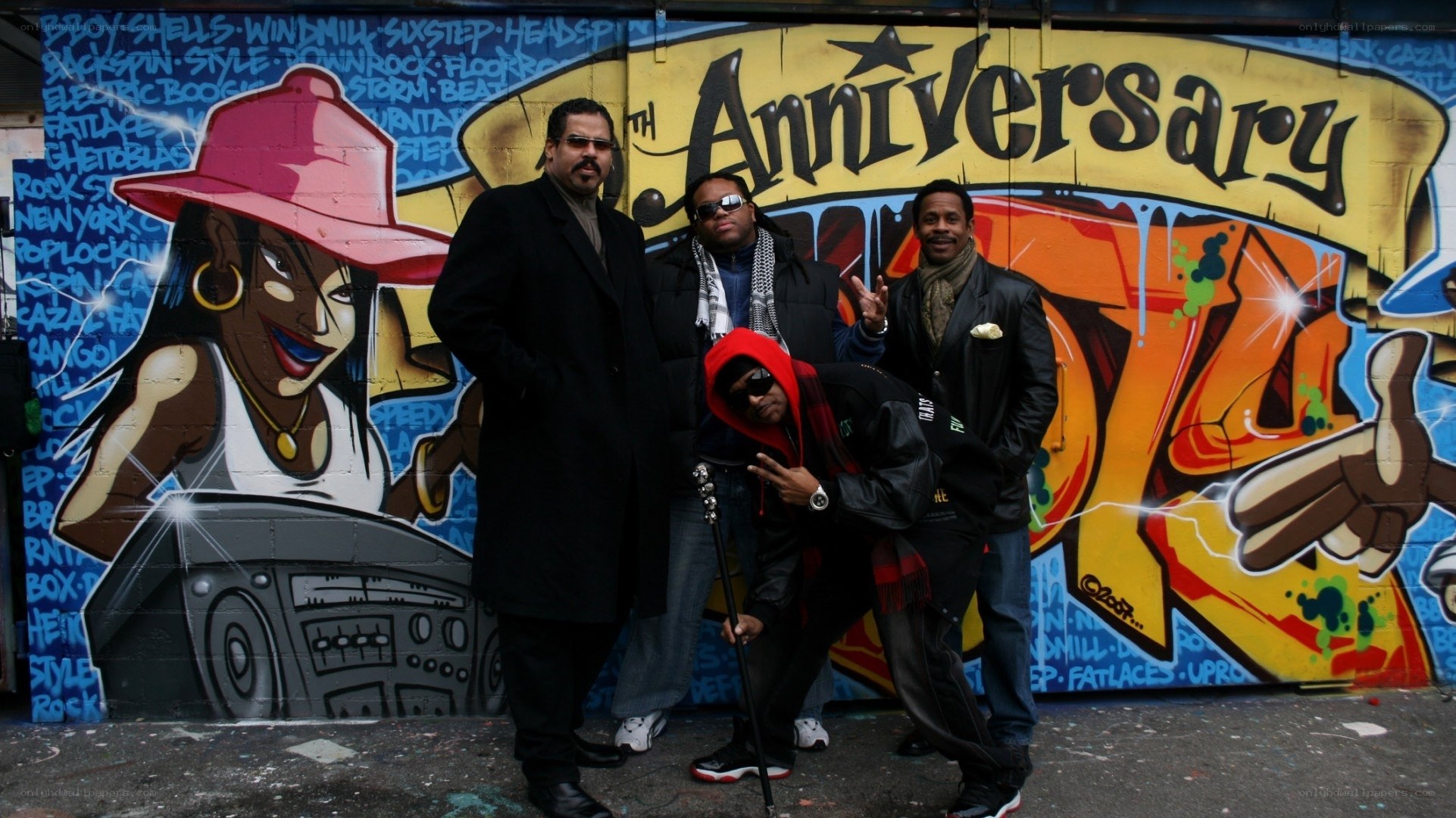 Four men pose in front of graffiti