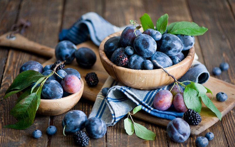 Fresh plums and berries on wood
