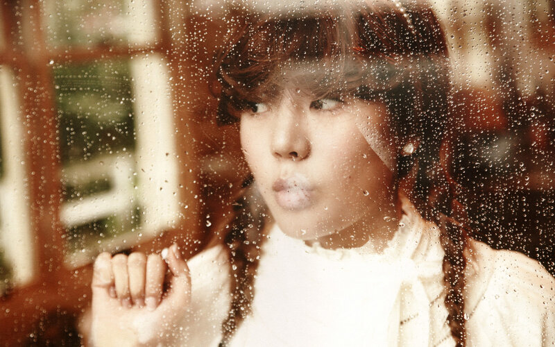 girl blowing bubble through rain-streaked window