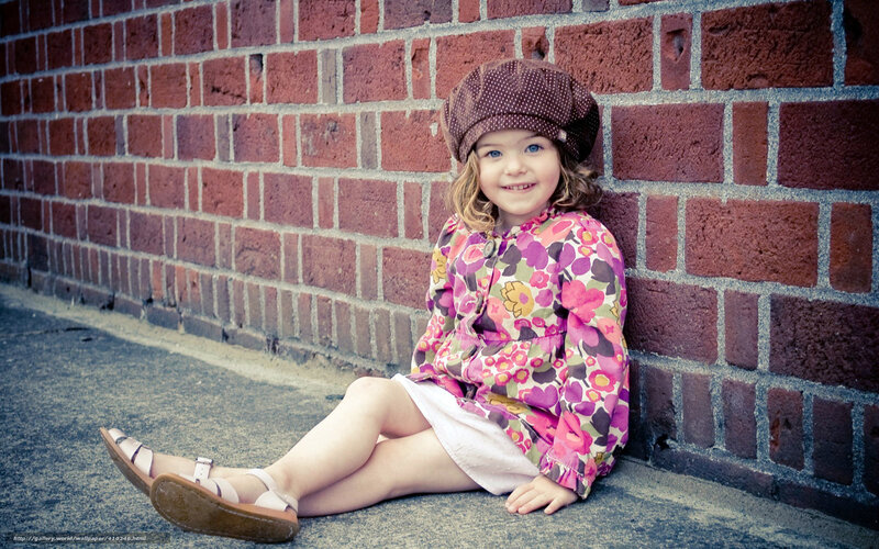 Girl in floral dress sitting by brick wall