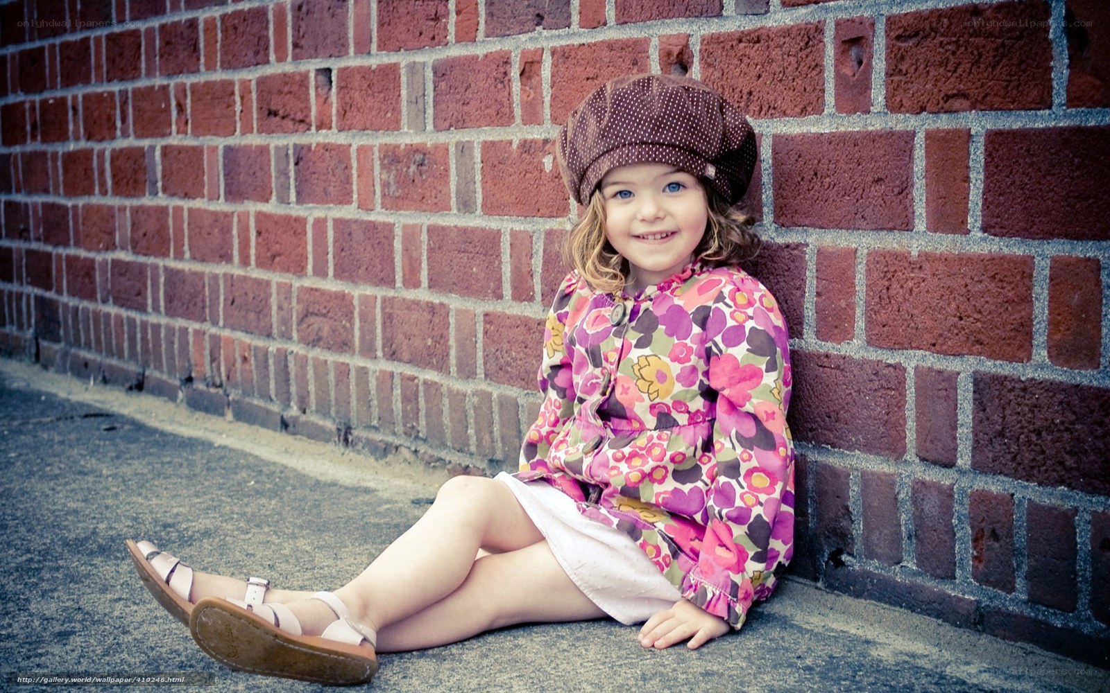 Girl in floral dress sitting by brick wall