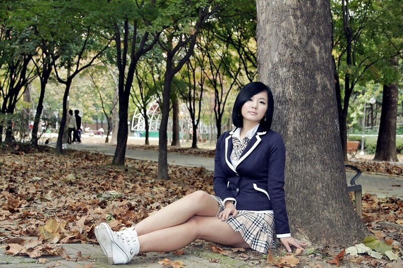 Girl in school uniform sitting by tree