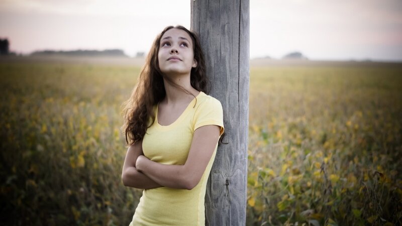 Girl leaning on post in field