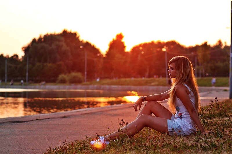 Girl sitting by the water at sunset