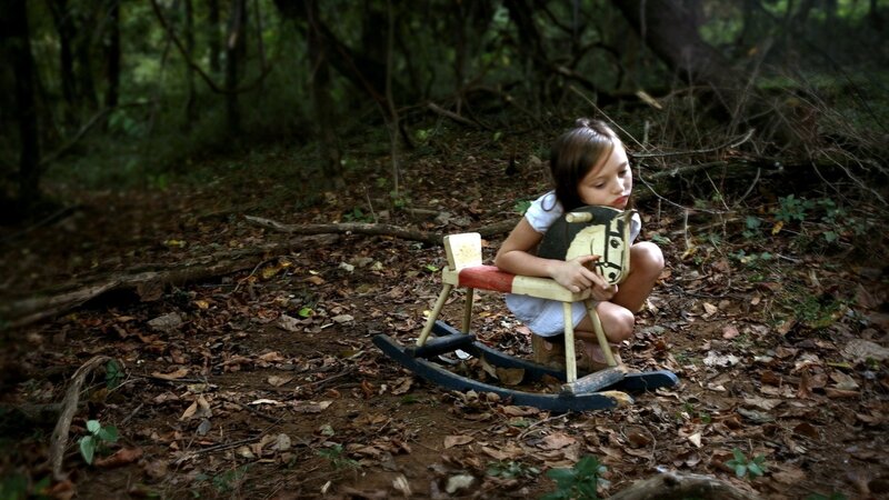 Girl with rocking horse in forest