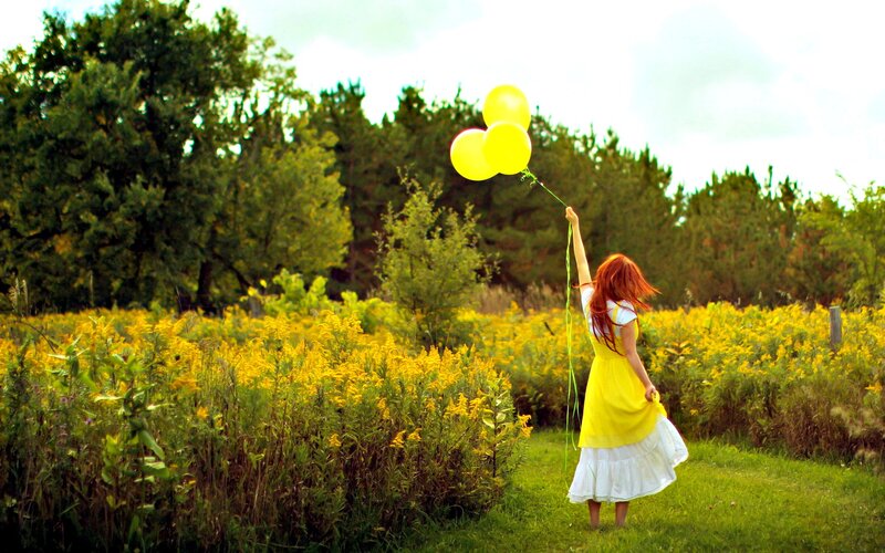 Girl with yellow balloons in field