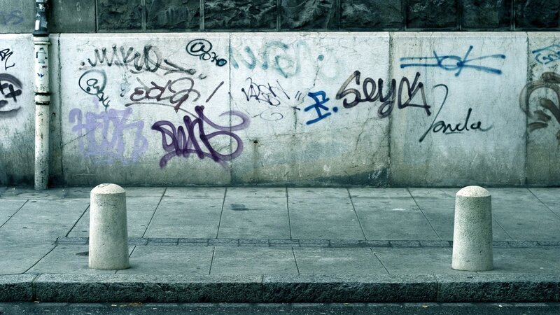 Graffiti-covered Wall — Gray, Dull, Photograph, Bollards, Sidewalk, Purple