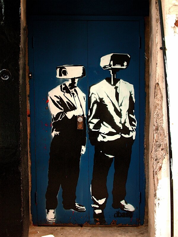 graffiti of two figures with cameras for heads