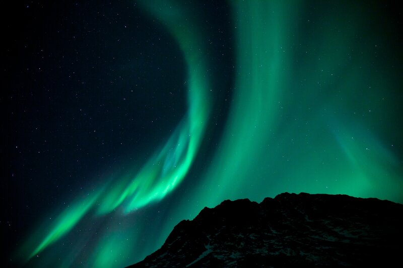 Green aurora over mountain silhouette