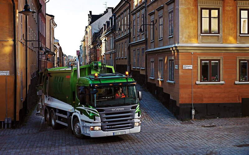 Green garbage truck in city street