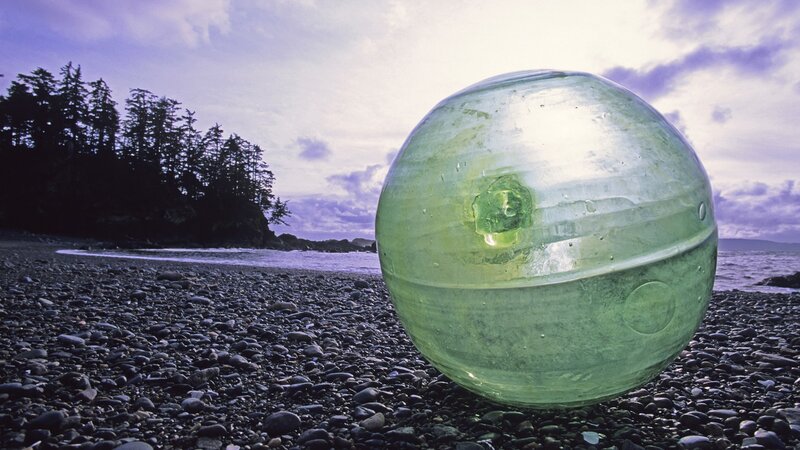 Green glass ball on pebble beach